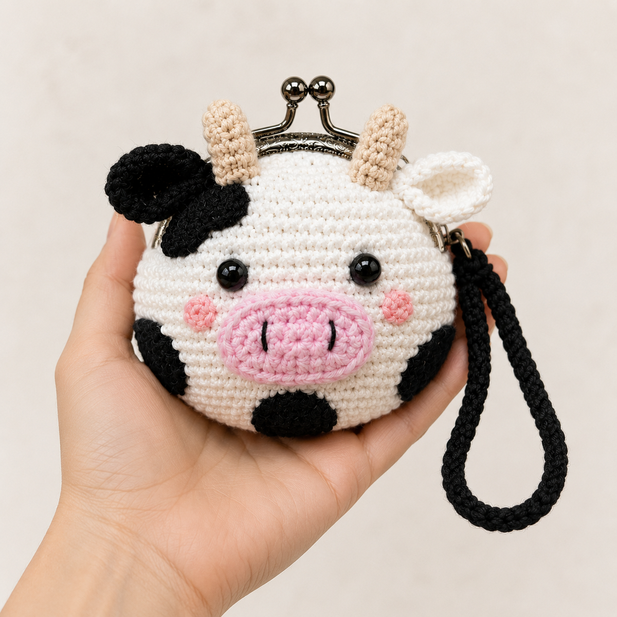Handmade crochet cow coin purse held in one hand for size reference
