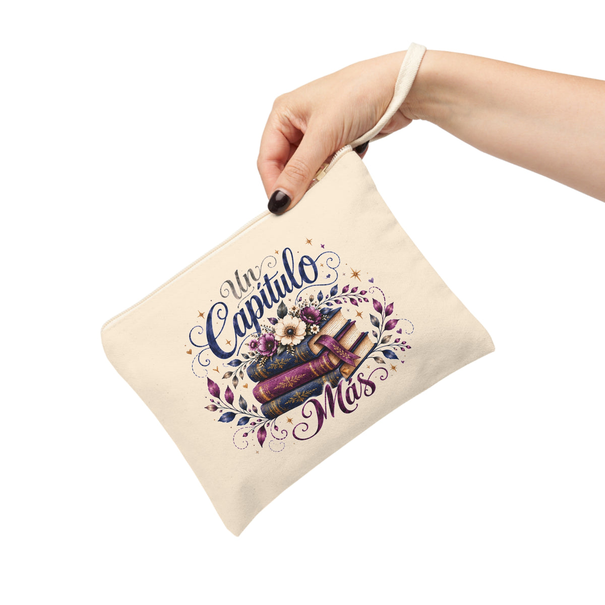 Hand holding an Un Capítulo Más canvas pouch with floral books design in navy, purple, cream and gold tones.