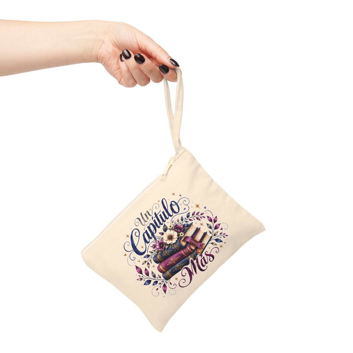 Un Capítulo Más canvas wristlet pouch shown hanging by its wrist strap, decorated with stacked books and flowers.